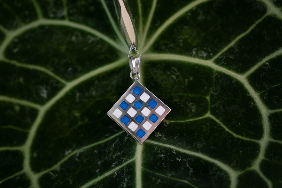 Blue and white checked enamel pendant on dark leaf