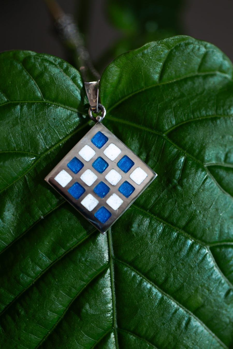 Blue and white checkered enamel pendant on a green leaf