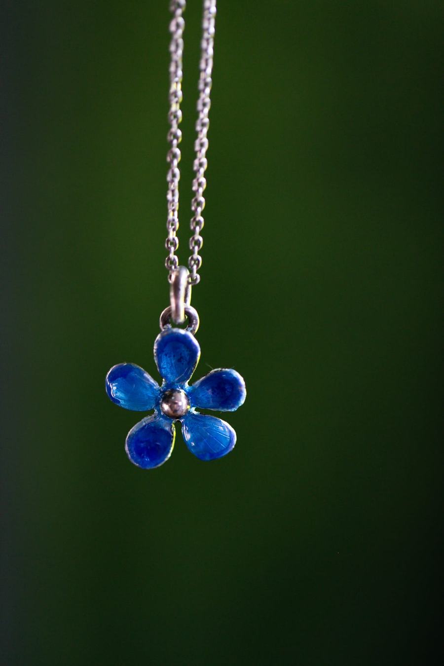 Blue enamel flower pendant on green background